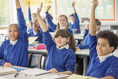 children with hands up in school