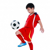 Young boy playing keepie uppies with a football. He is wearing a red football kit.