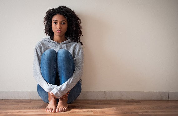 young girl sat sadly against a wall