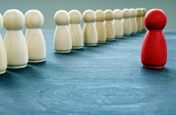 A line of white wooden figures and one red wooden figure