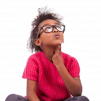 A young child sitting with crossed legs and looking quizzical.