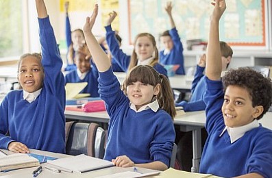 Children in school uniforms with their hands up