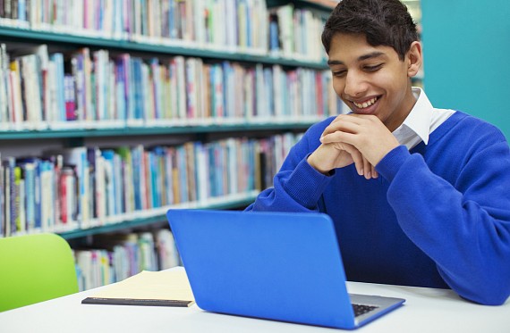 A secondary aged boy in school uniform looking at a laptop