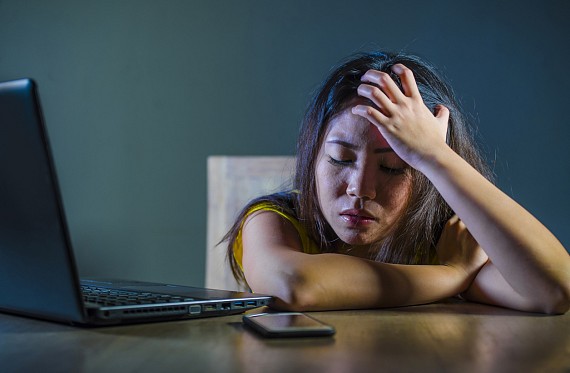 a young person with their head in their hand looking upset by a laptop